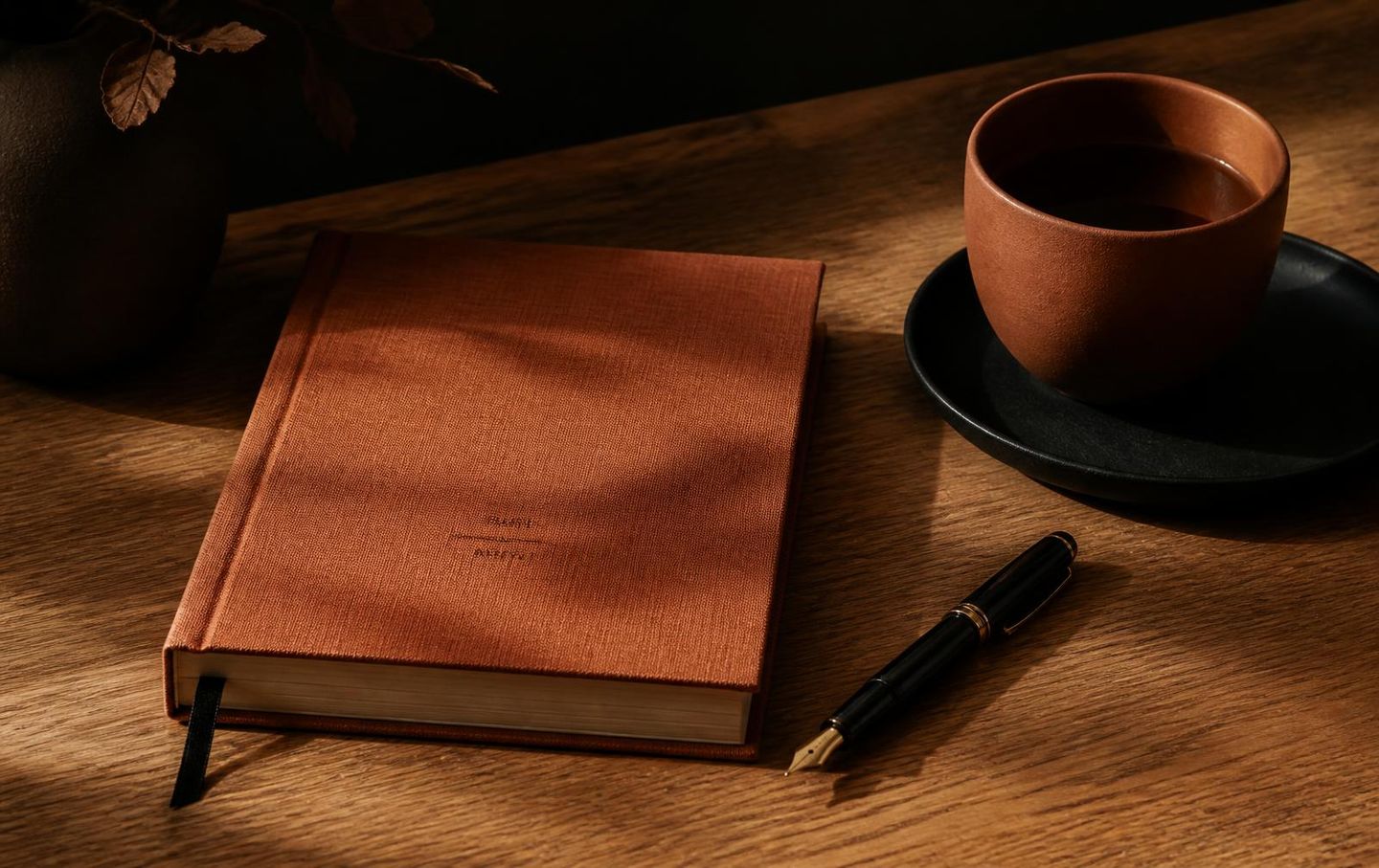 Carnet relié terracotta, stylo plume et tasse posés sur un bureau en bois